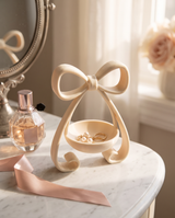Coquette bow jewellery dish holding gold rings and pearl earrings on a vanity