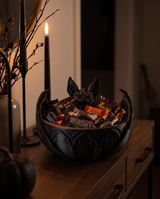 Gothic bat candy bowl filled with sweets beside a black taper candle